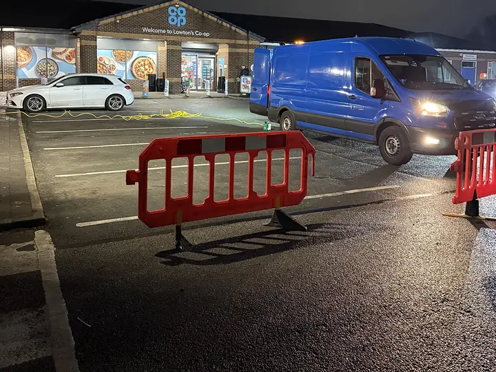 Safety barriers around commercial drainage work in a shop car park at night