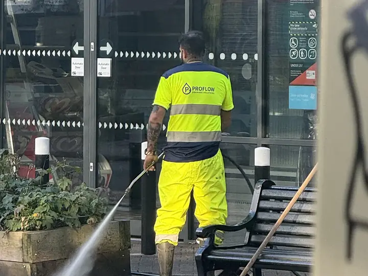 Pro Flow operative in branded hi-vis jet washing the paving outside a shop entrance